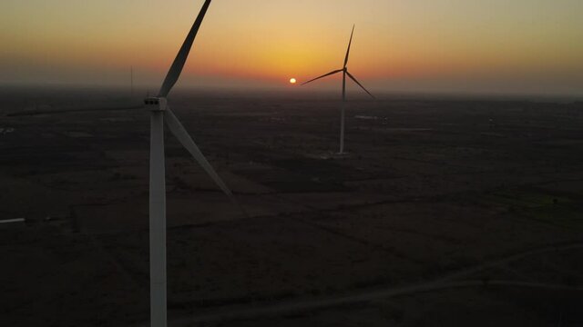 Large wind turbines with blades in field aerial view bright orange sunset