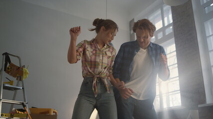 Joyful family enjoying improvement of apartment. Happy couple dancing indoors.