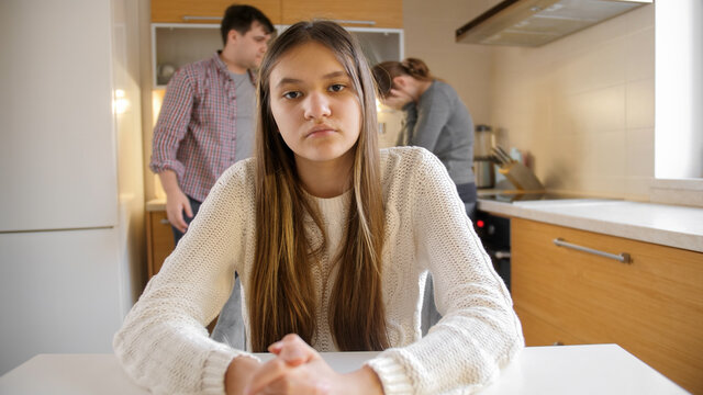 Teenage girl looking in camera while parents arguing and having conflict on kitchen. Family violence, conflicts and relationship problems