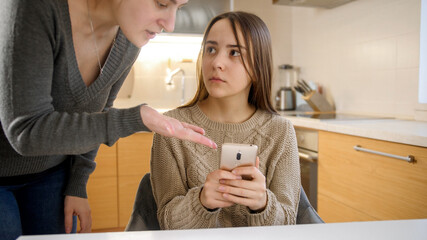 Teenage girl crying after mother shouting at her and taking away smartphone. Gadget addiction and...