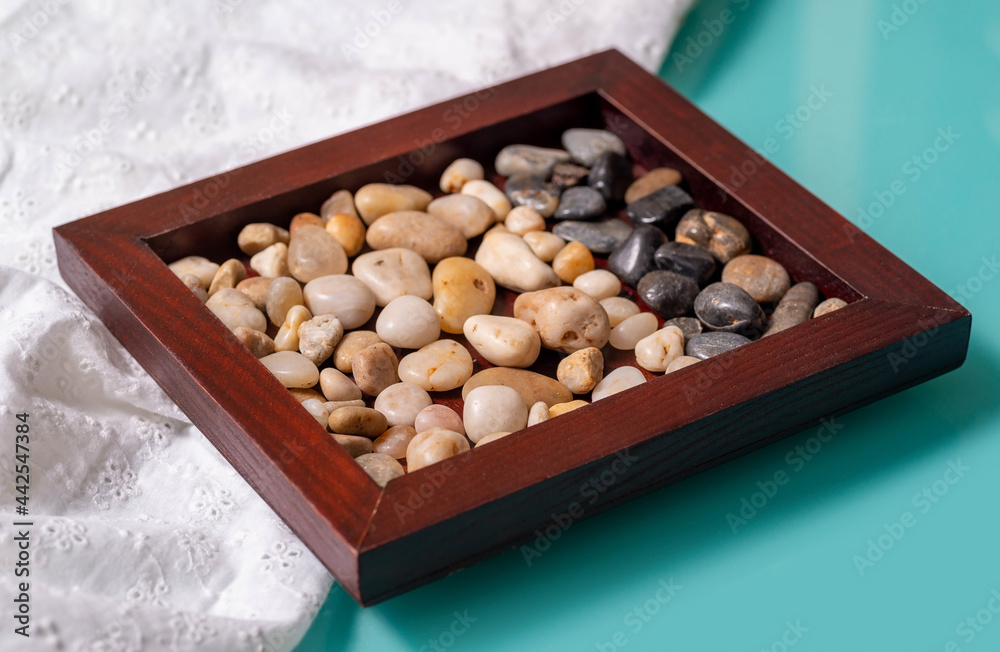 Wall mural a wooden frame with two colors of sea pebbles on a turquoise table with a white cloth.