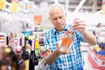 old age man examines bottle of vermouth in alcoholic section of supermarket