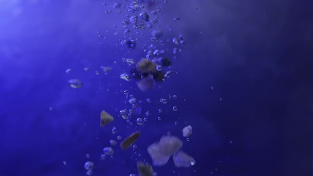 Close up of large gem stones falling into fish tank in slow motion, bubbles flow up, textured background with blue lighting, shallow depth of field