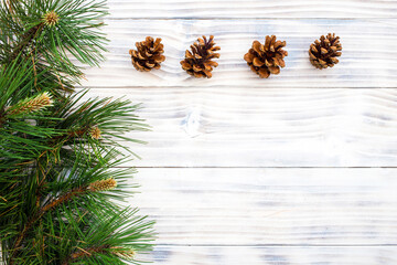 Four fir cones with pine branch on white wooden background.
