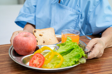 Asian senior or elderly old lady woman patient eating breakfast vegetable healthy food with hope and happy while sitting and hungry on bed in hospital.