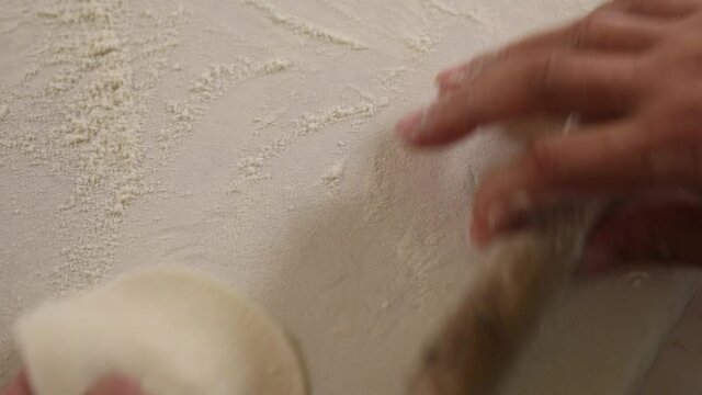 Close up shot of a professional chef using a small roller to flatten dumpling dough.