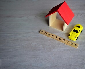 Selective focus image of toy house, toy car and wooden cube with text MORATORIUM. Copy space for...