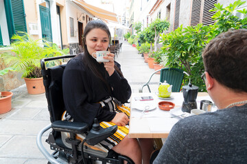 Happy disabled woman wheelchair drinking coffee with boyfriend on restaurant terrace