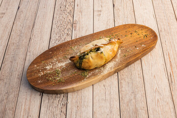 Argentine empanada of wheat flour overflowing with stew filling with spinach on wooden plate
