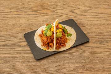 Mexican tacos with wheat tortillas with guacamole, pineapple chunks and pulled pork on black slate...