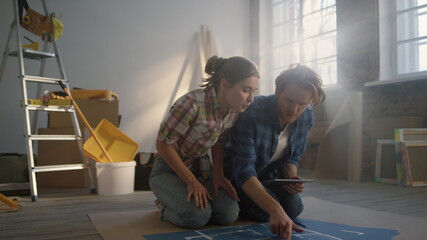 Fototapeta premium Couple studying scheme on floor. Family making home repair plans on tablet.