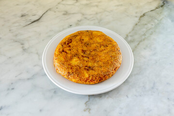 Spanish omelette with lots of juice served on a white plate on a white marble table