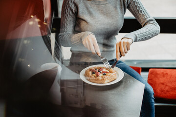 The girl cuts the bun. Lunch at the coffee shop. Delicious fresh pastries with berries and fresh coffee. Snack in a cafe