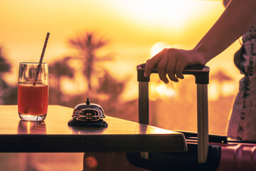 Woman with suitcase ringing hotel service bell with sea and palm tree view on sunset. Travel...