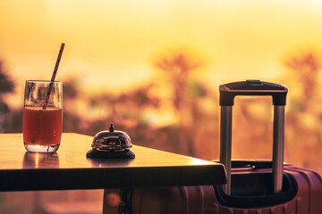 Suitcase, ringing hotel service bell with welcome drink and sea, palm tree view on sunset. Travel...