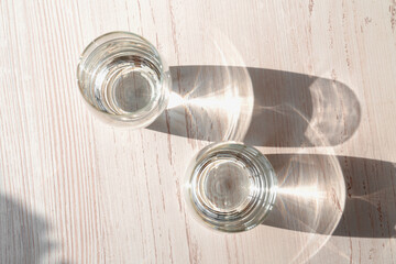Two glasses of water on white wooden background under direct sun shines. Top view of glasses water....