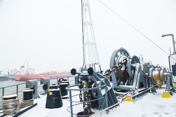 The mooring deck of a cargo ship with anchor winches, an anchor chain on winches, bollards and haws with mooring ropes, frozen and covered in snow. Snow on the mooring deck of a cargo ship.