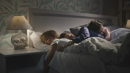 Young attractive mother reading book with fairy tales for children, daughters before sleeping in the bed. Woman and two girls getting ready for good night. Bed time together. Slow motion shot. - Powered by Adobe