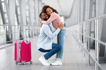 Happy black man hugging girl kid in airport - obrazy, fototapety, plakaty
