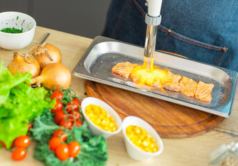 Young chef fries salmon fish with a gas burner in a modern kitchen. The man prepares food at home. Cooking healthy and tasty food.