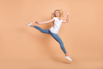 Photo of cute adorable young woman dressed white t-shirt jumping high walking waving arm smiling isolated beige color background