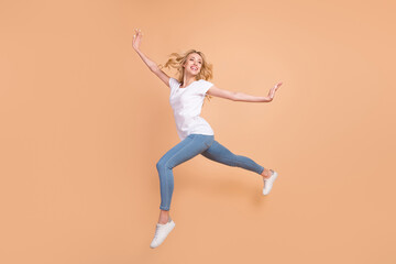 Fototapeta na wymiar Photo of pretty sweet young woman dressed white t-shirt jumping high walking smiling isolated beige color background