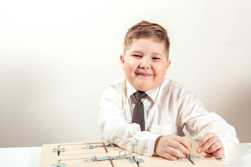 Naklejka premium boy of 7-9 years old plays a board game, sits at a table in a light shirt against the background of a white wall. Happy child studying at school