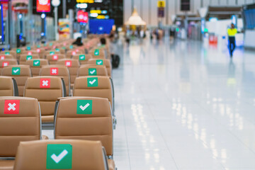 Rows empty brown chairs with the sticker sign sitting position for social distancing in waiting terminal of the airport to prevent of Corona virus (Covid-19). Safe travel new normal social distancing.