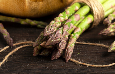 A bunche of a fresh asparagus covered in water drops close up on a dark wood background