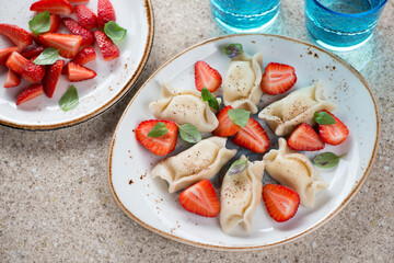 Plate of curd dumplings or vareniki served with fresh strawberry, horizontal shot on a beige marble background