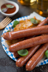 Closeup of smoked sausages with sauerkraut on a blue and white carton disposable plate, vertical shot