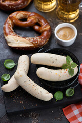 Weisswurst or german white sausages on a black wooden serving board and pretzels, studio shot, selective focus