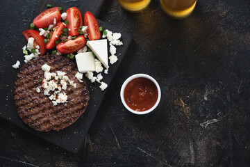 Grilled balkan pljeskavica, red tomatoes and bryndza cheese, flatlay on a dark brown stone background, horizontal shot with copy space