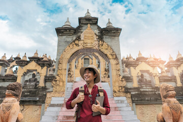 Portrait Asian man backpacker travel pagoda in southeast Asia. Traveler happy smile during backpack and wearing a hat carrying a backpack travel at Buddhist temple.