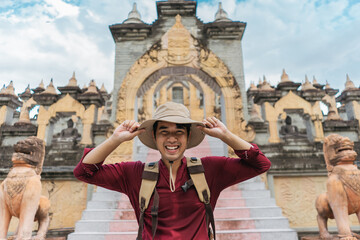 Portrait Asian man backpacker travel pagoda in southeast Asia. Happy traveler wearing a hat carrying a backpack on a Buddhist temple.