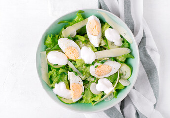 Salad with eggs, lettuce, cheese, cucumber, white radish and scallion topped with yogurt served in the bowl on the white table. Top view