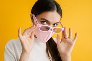 Young brunette woman in face mask and sunglasses looking at camera
