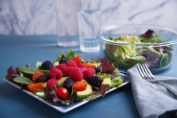 Salad with red berries, cherry tomatoes and avocado, on a blue table.