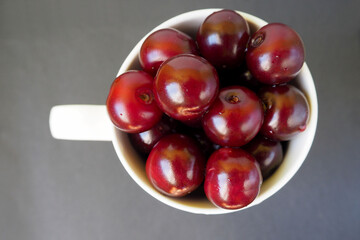 a white mug filled with ripe cherries stands on a gray background. view from above