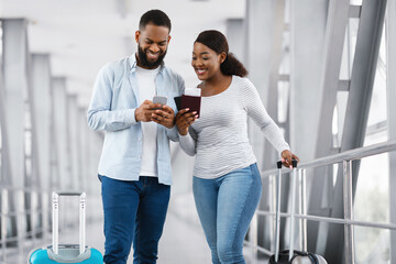 Happy black couple using phone at airport