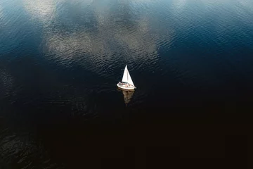 Wandaufkleber Aerial view of tiny yacht with white sails floating in calm ocean with no wind. © Tadas