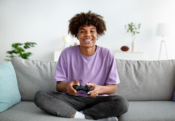 Home entertainments. Happy black teenager with joystick playing online computer games in sofa indoors, full length © Prostock-studio