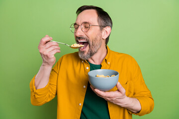 Photo of charming cute mature man dressed orange shirt glasses smiling eating cereals isolated...