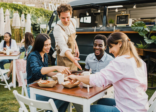 Multiracial people having fun eating at food truck outdoor - Focus on left girl face - Powered by Adobe