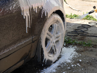 Hand wash the car with water and shampoo, the water jet is directed at the wheel