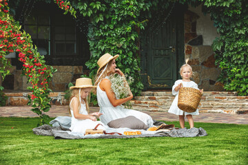 Young adult beautiful woman in a dress with children on a picnic in the garden at home
