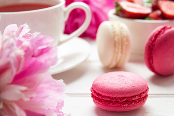 Macarons with strawberries, fruit tea and peonies close-up on a white wooden table. Selective focus