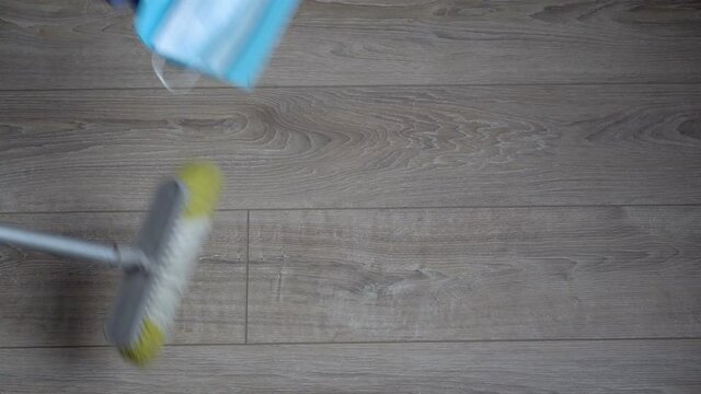 A male cleaner sweeps a used disposable face mask onto a dustpan. Covid-19 waste. The concept of cleaning up the environment after the coronavirus pandemic. Top view. Close-up. Faceless. 4K.