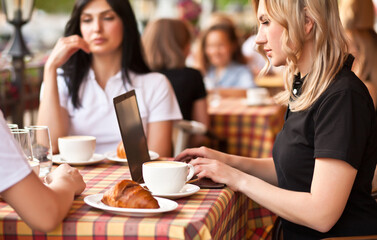 Beautiful women workers or students using laptop at cafe and talking