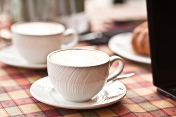 Cups of cappuccino coffee with croissant in a cafe